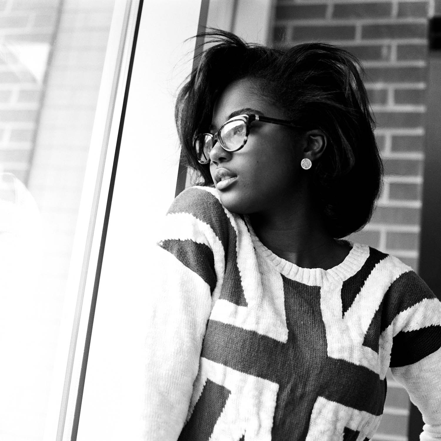 Black and white film portrait of a girl in a window wearing a british flag shirt. Photographed on a Hasselblad 500c