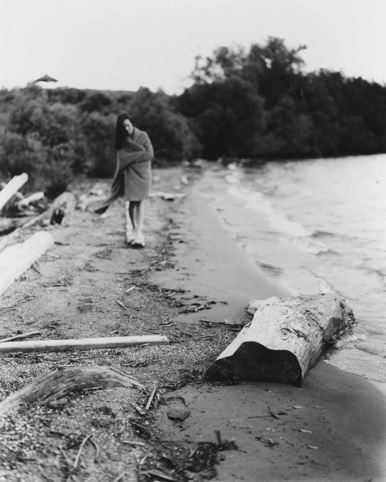A 4x5 film portrait of a girl on a beach with driftwood