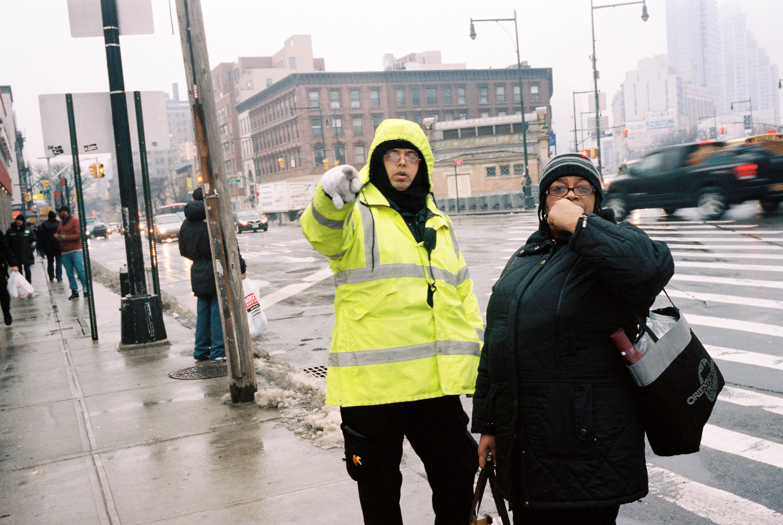 A NYC public servant in yellow rain attire points something out to a tourist