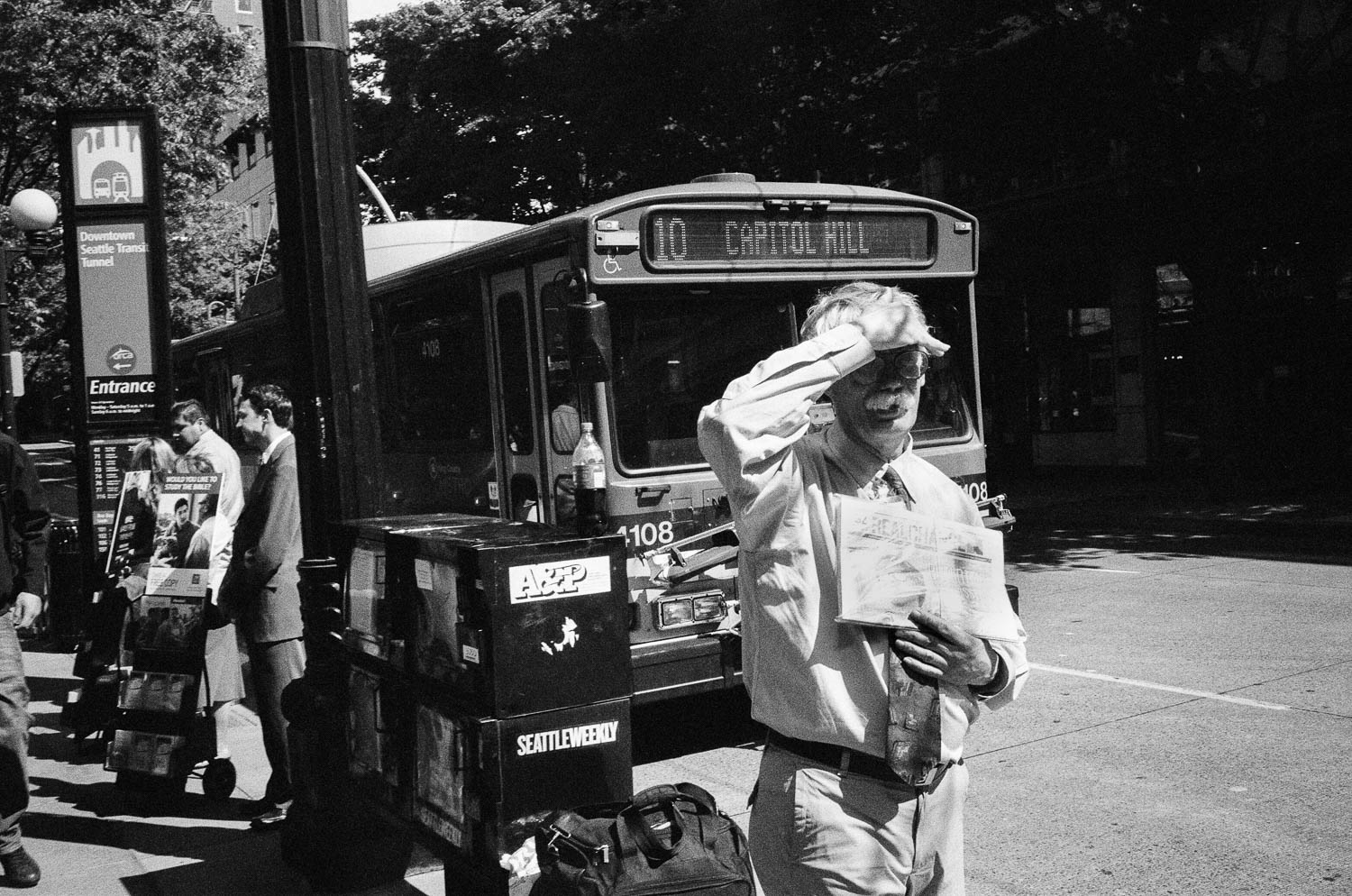 A Seattle man shielding his eyes from the sun while holding a newspaper in front of a city bus