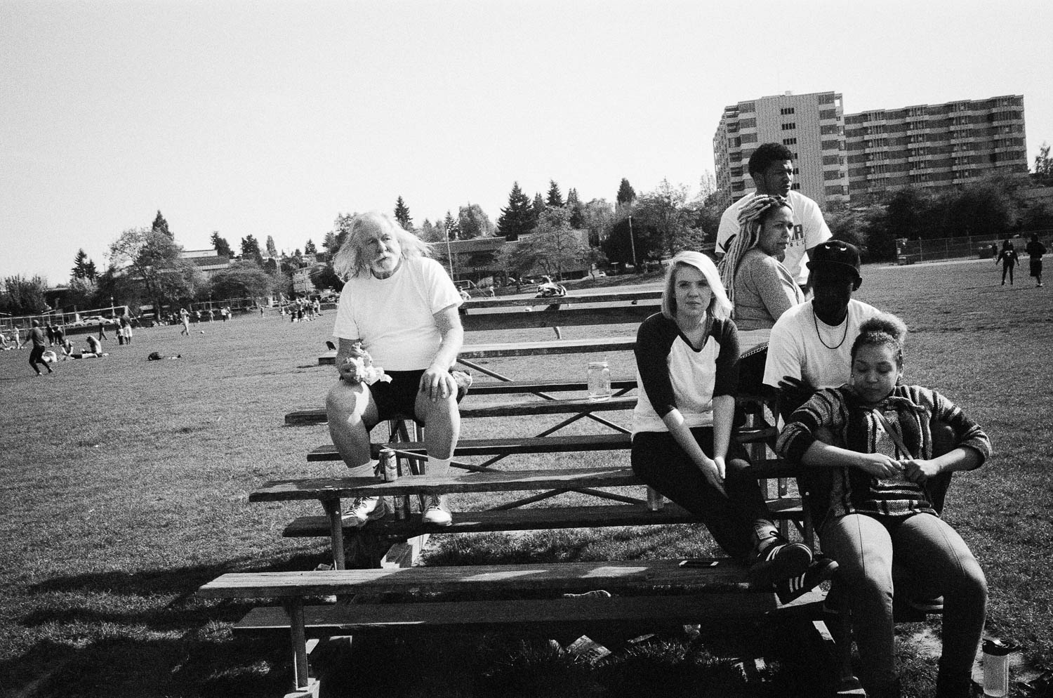 An older man sitting on one end of the bleachers, and a group of kids sitting at the extreme opposite end