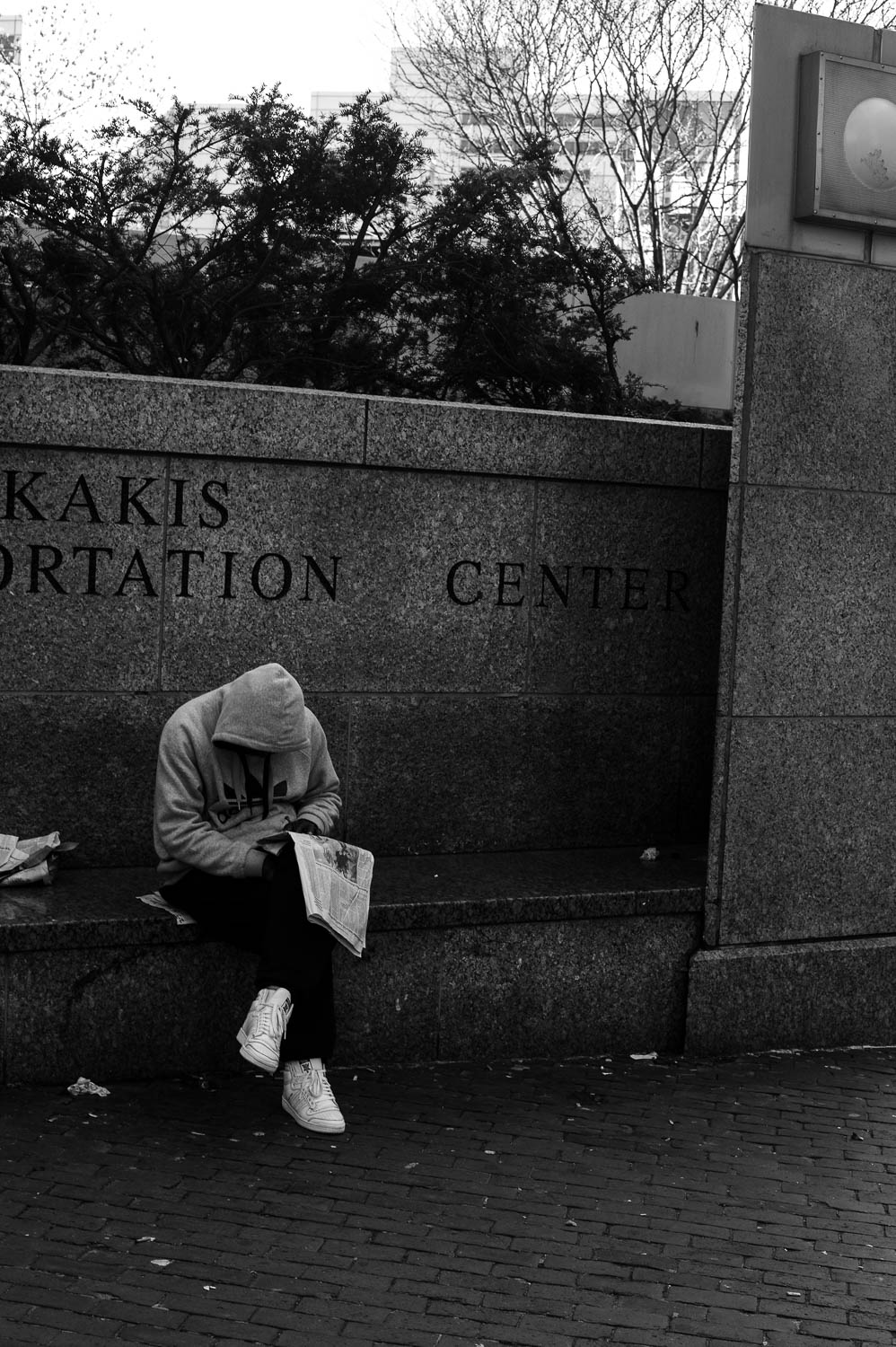 A man wearing a hood slumps over a newspaper in Boston