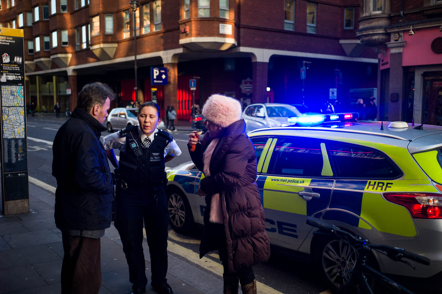 A London police officer chatting with a woman eating orange slices in a furry hat