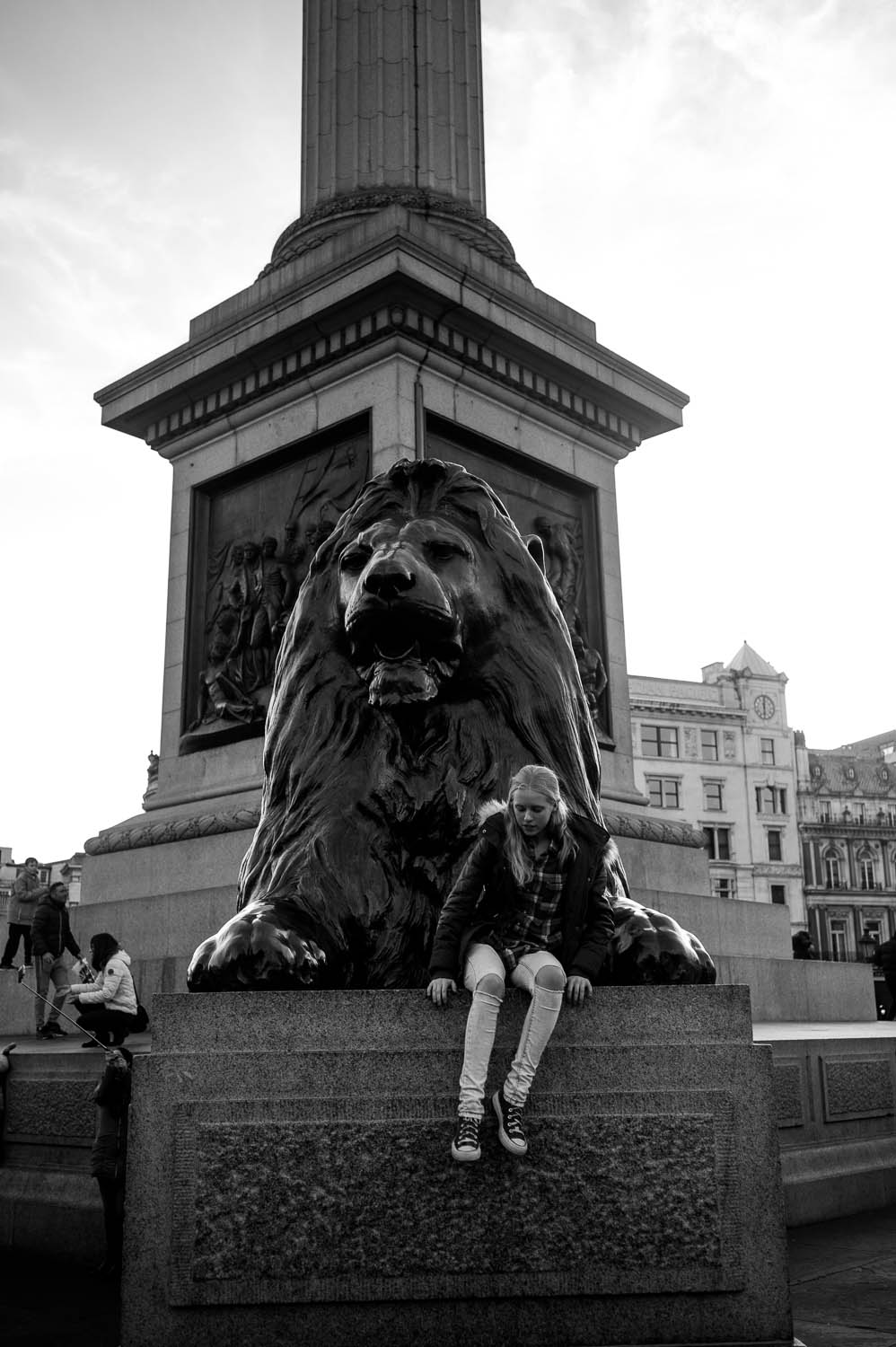 A girl sites in front of a lion statue in London
