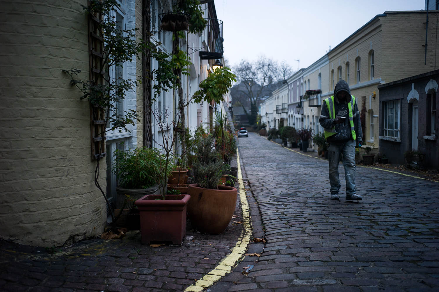 A worker in a reflective vest walks through a cobblestone street in London