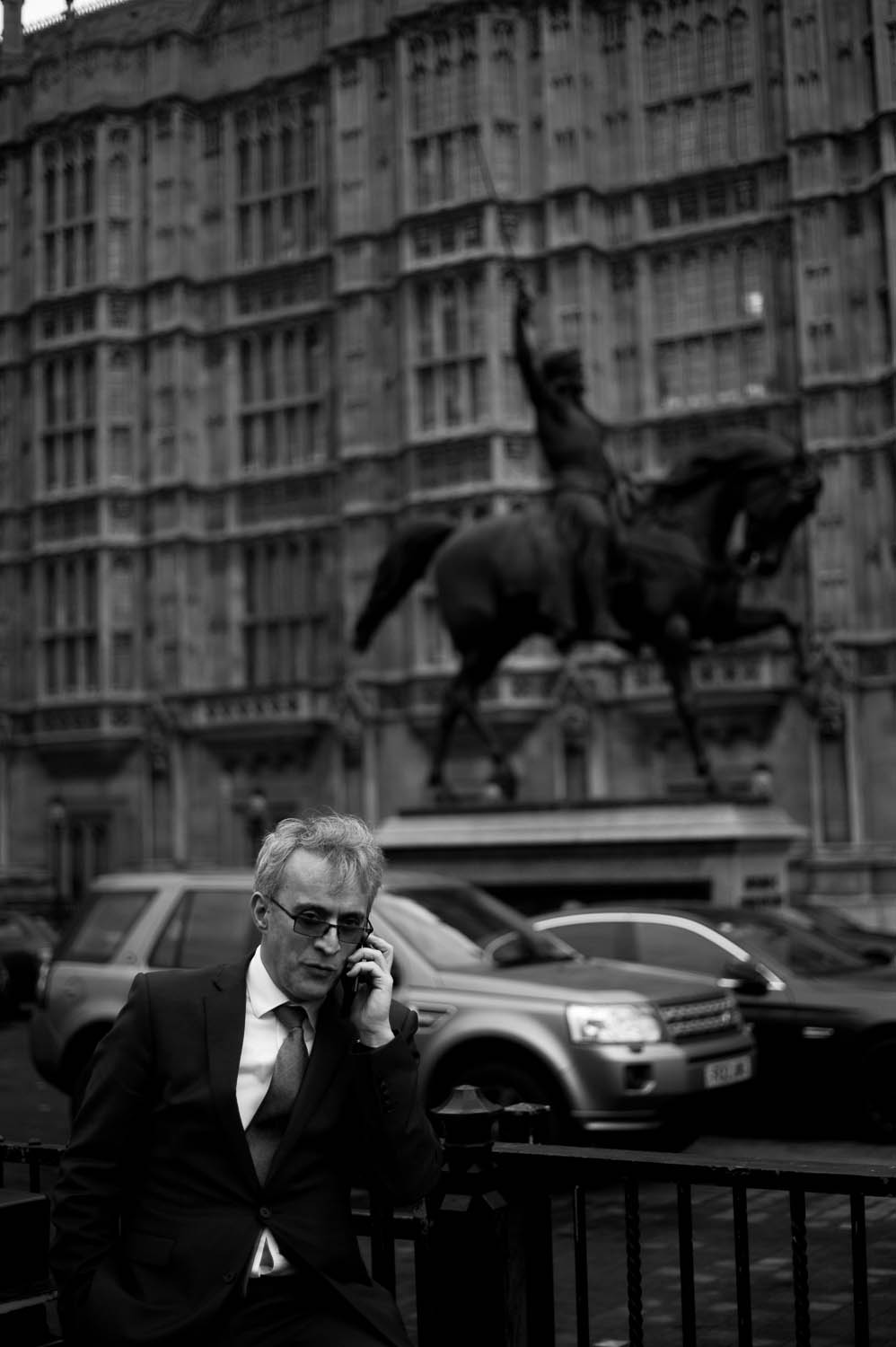 A man in a suit speaking on the phone in front of a horse statue in London