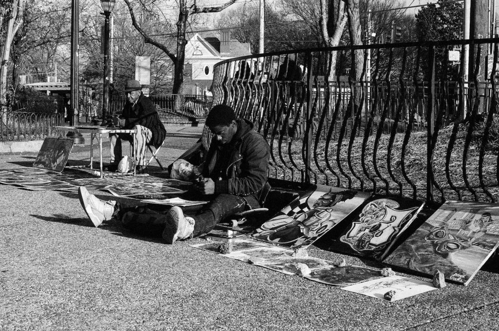 A young man sitting on a skateboard and selling paintings in Atlanta, Georgia